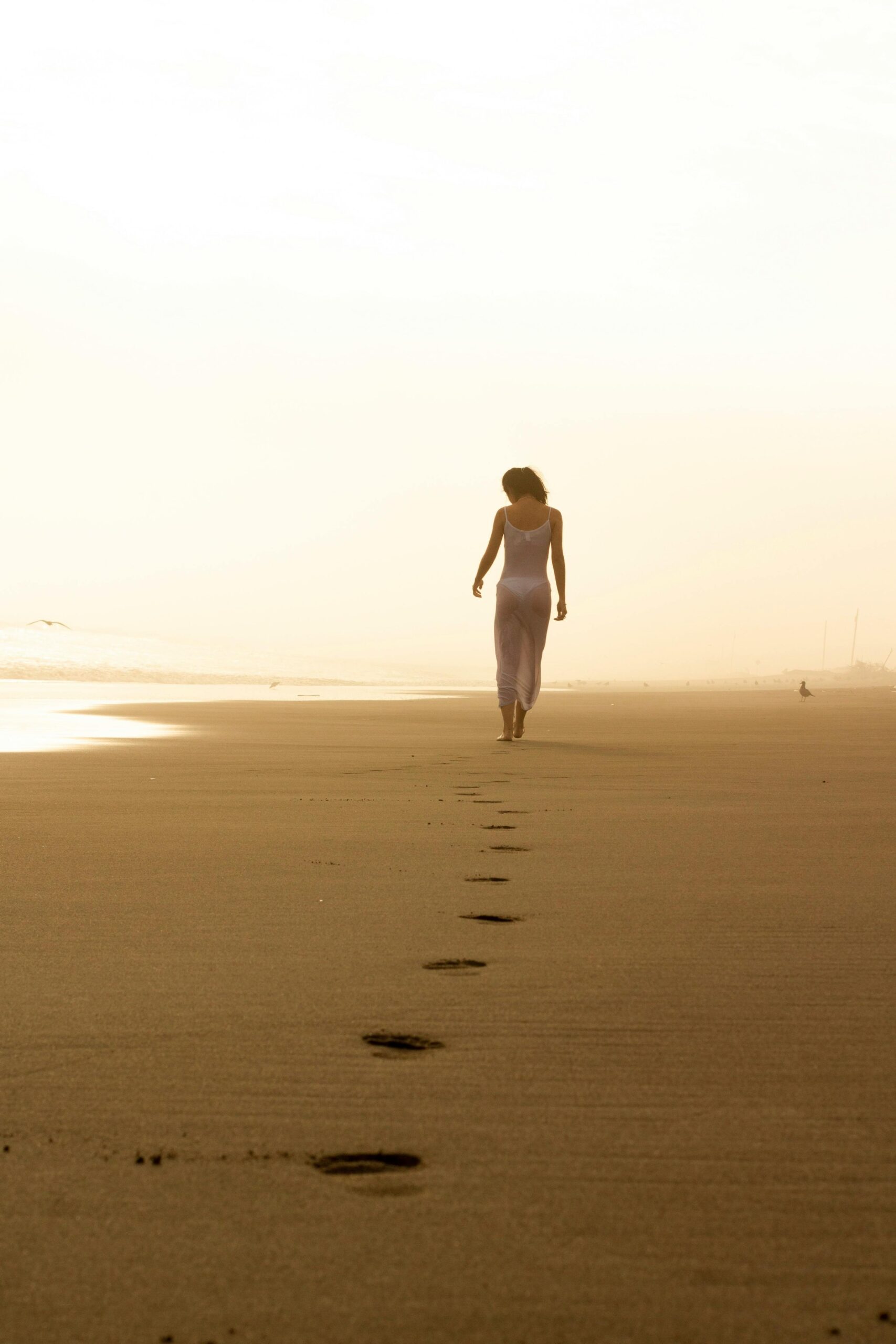 Walking forward on a beach leaving footprints behind, symbolizing letting go of shame and guilt in recovery